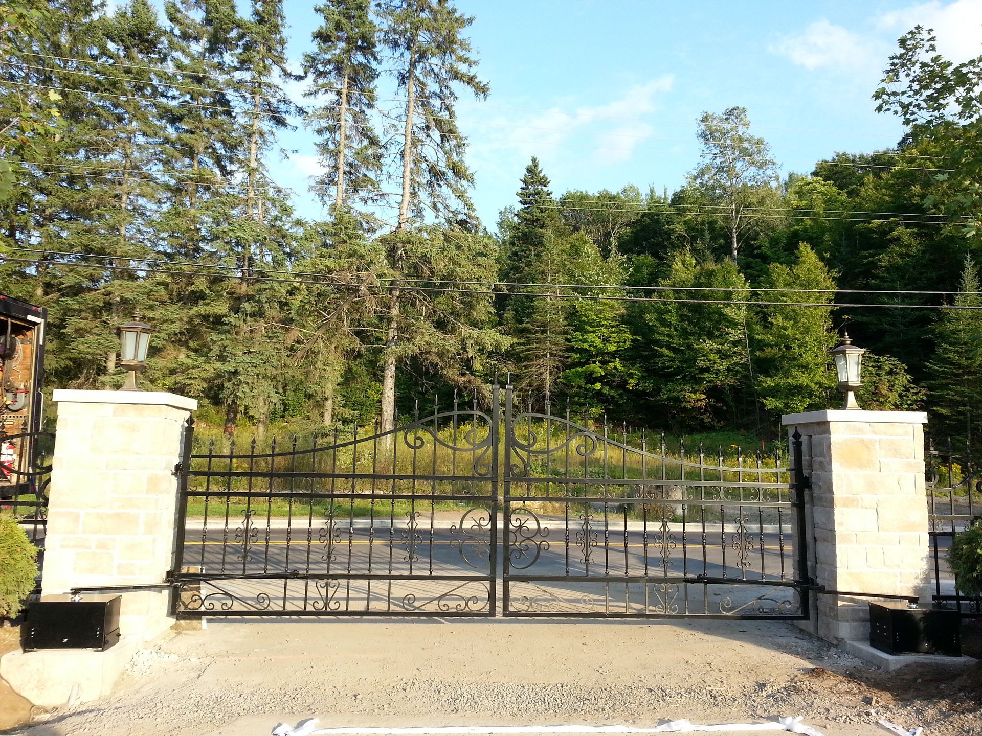 Un portail en fer forgé s'ouvre sur une allée avec des arbres en arrière-plan