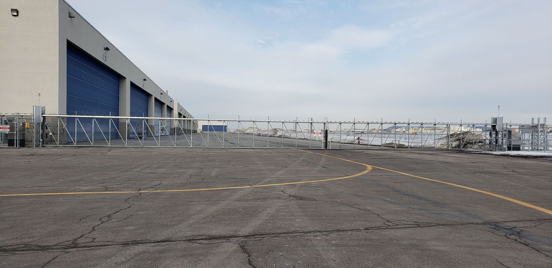 Un parking vide avec une clôture et un bâtiment en arrière-plan.