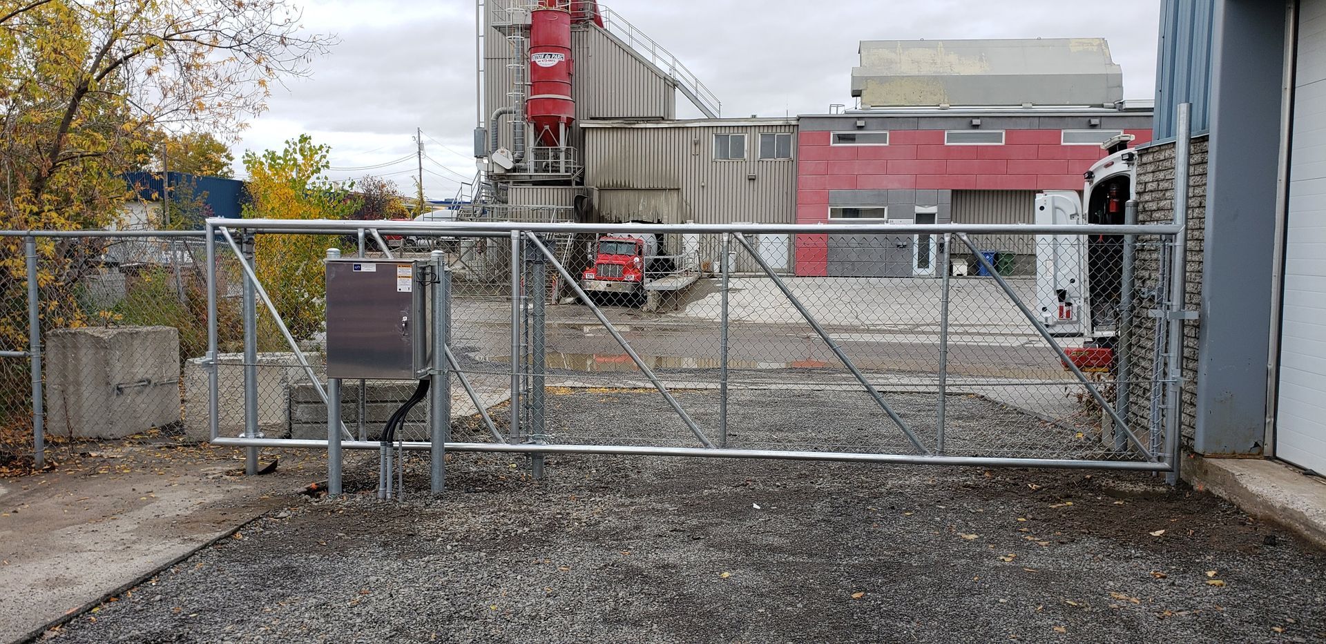Un portail métallique est ouvert sur une allée de gravier devant un bâtiment.