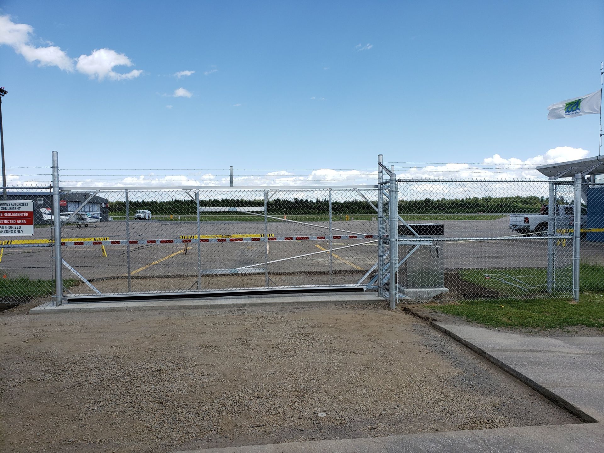 Un portail coulissant avec une clôture à mailles losangées devant un parking.