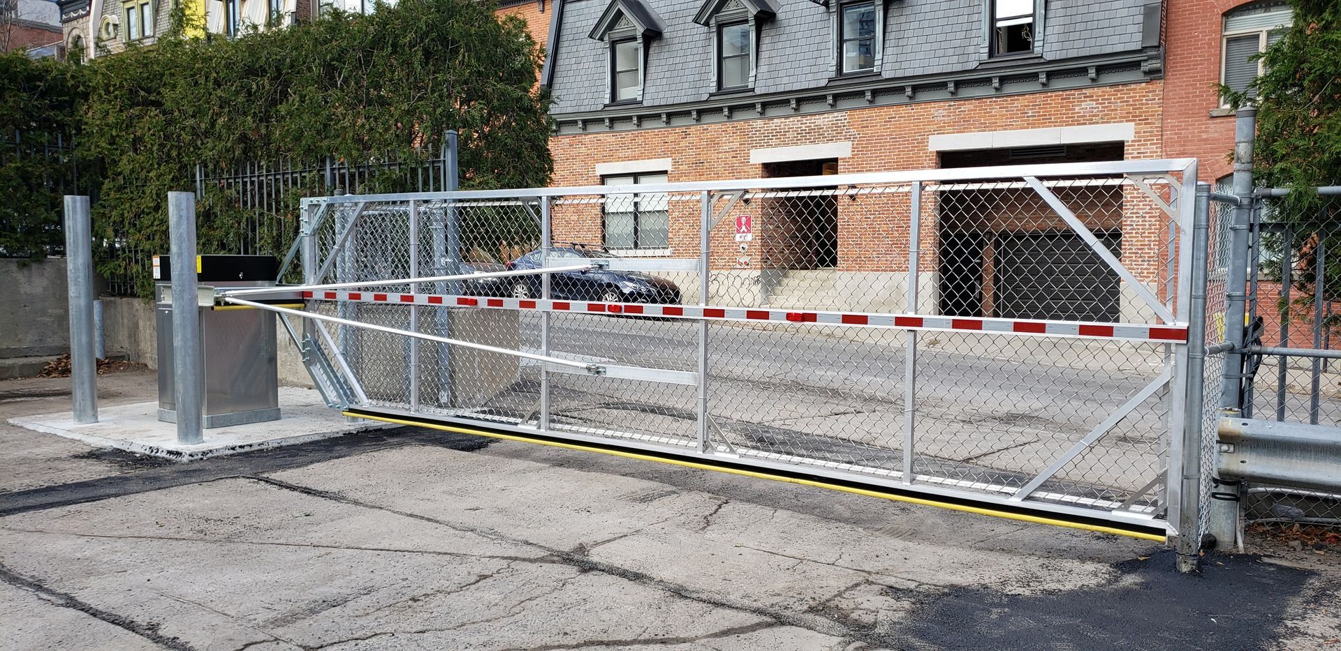 Une clôture bloque un parking devant un bâtiment en briques.
