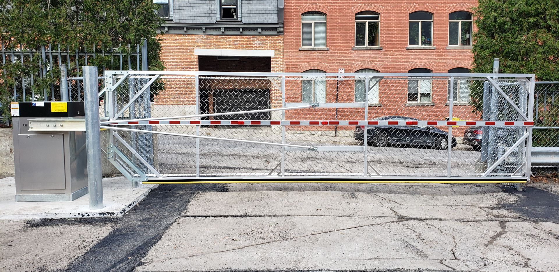 Un portail coulissant est fermé devant un bâtiment en briques.