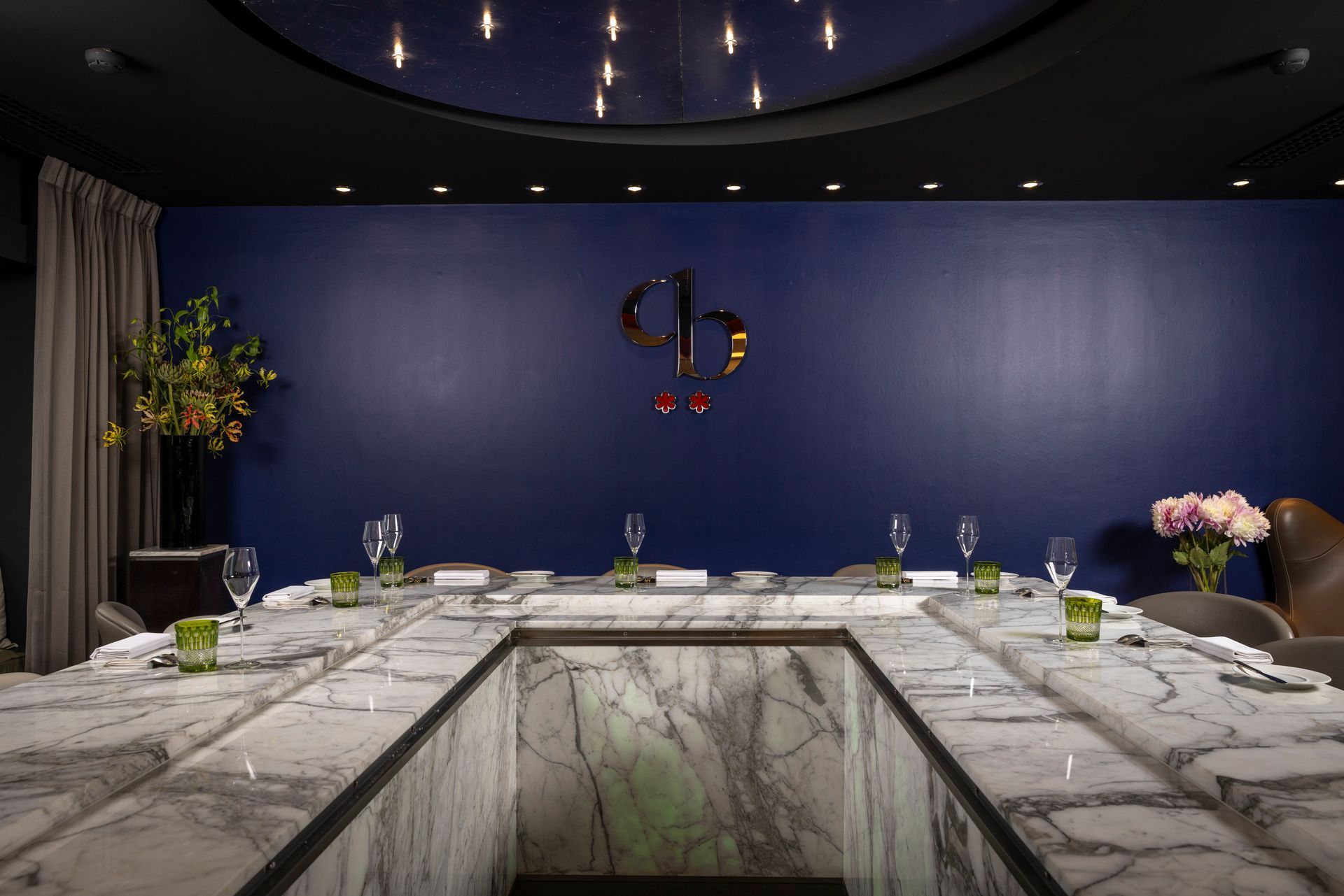 Formal dining room with marble table, blue wall with logo, and place settings.