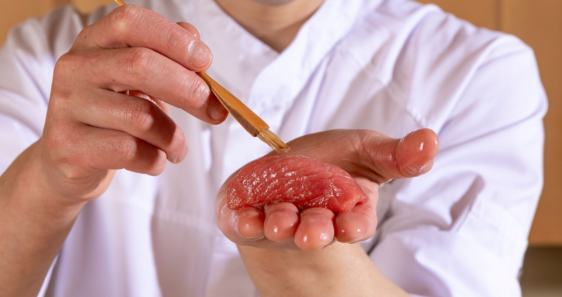 Chef slicing fish on a white countertop in a Japanese restaurant. Wooden wall backdrop.