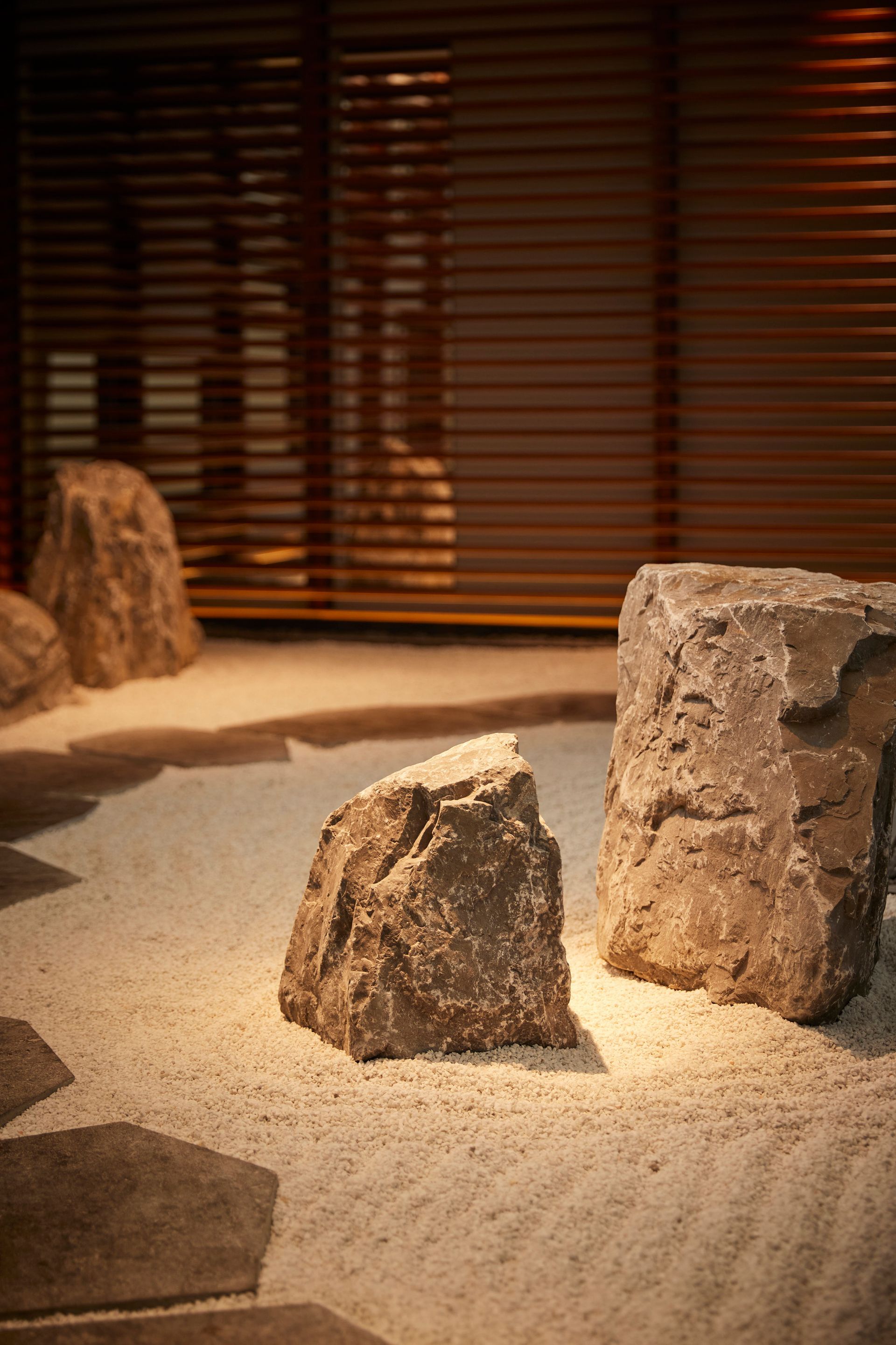 Zen garden with sand, large rocks, and wooden blinds in the background.