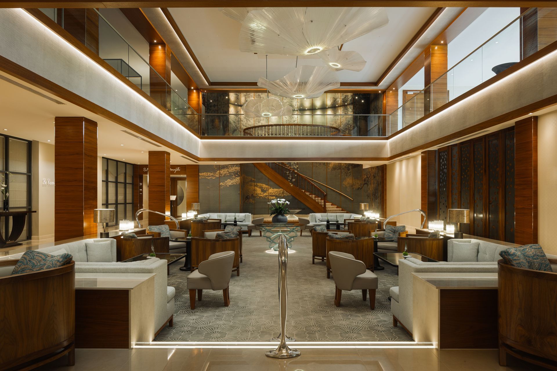 Lobby with seating, wood accents, and chandelier. Two-story with stairs leading up, neutral tones, modern design.