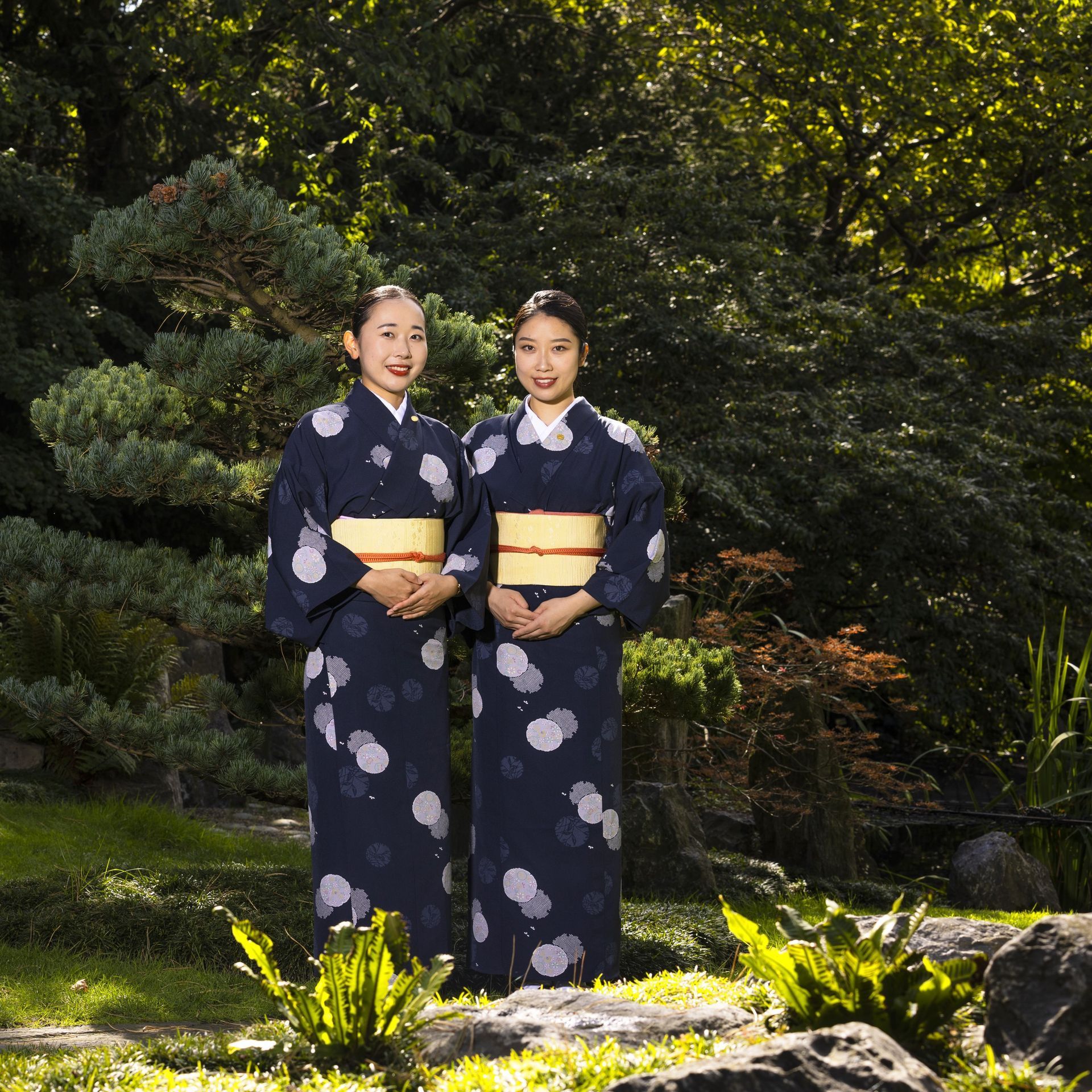 Two people in navy blue yukata pose in a garden.
