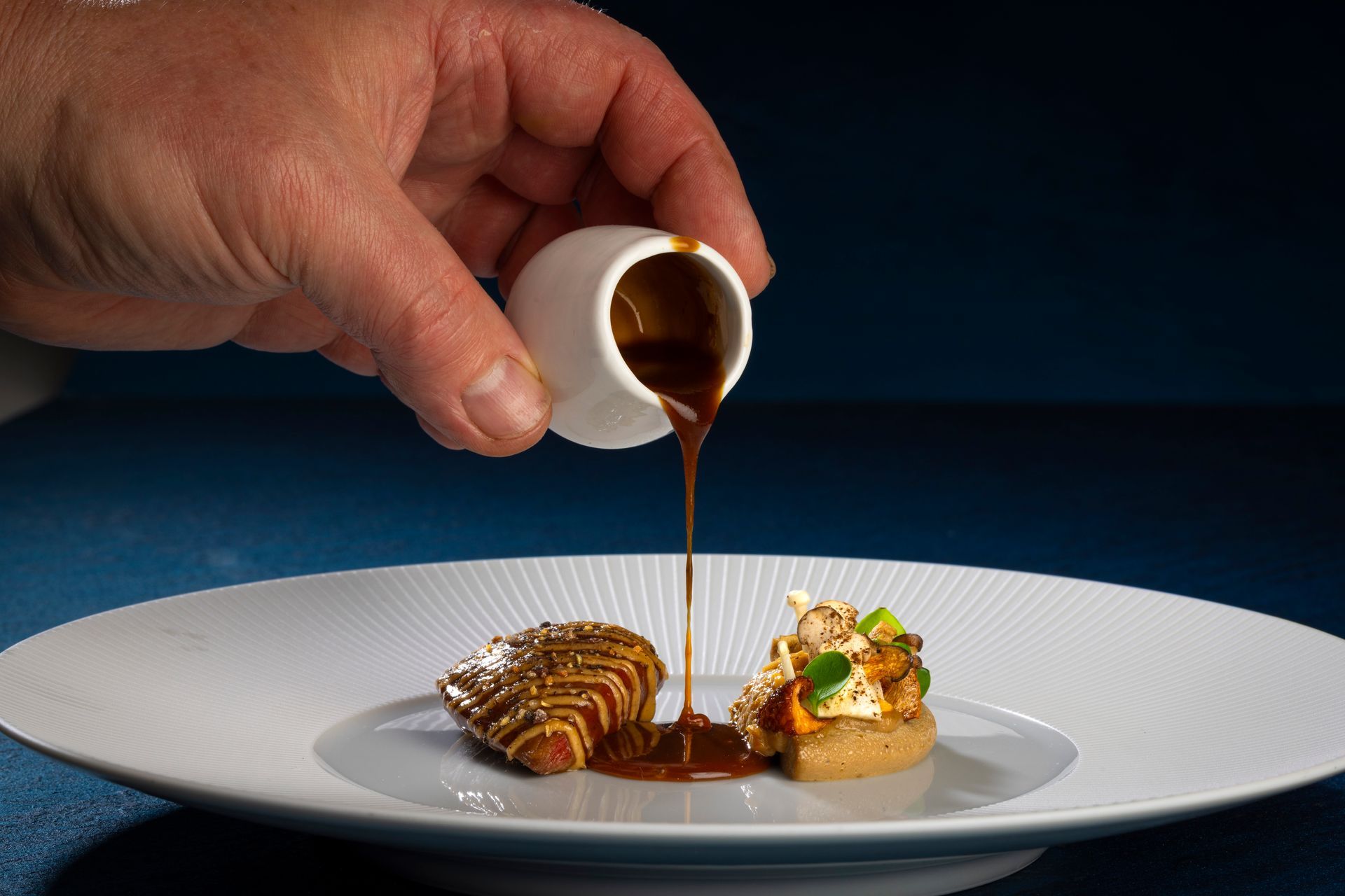 Waiter serving artfully plated food to a smiling diner in a fine dining restaurant.