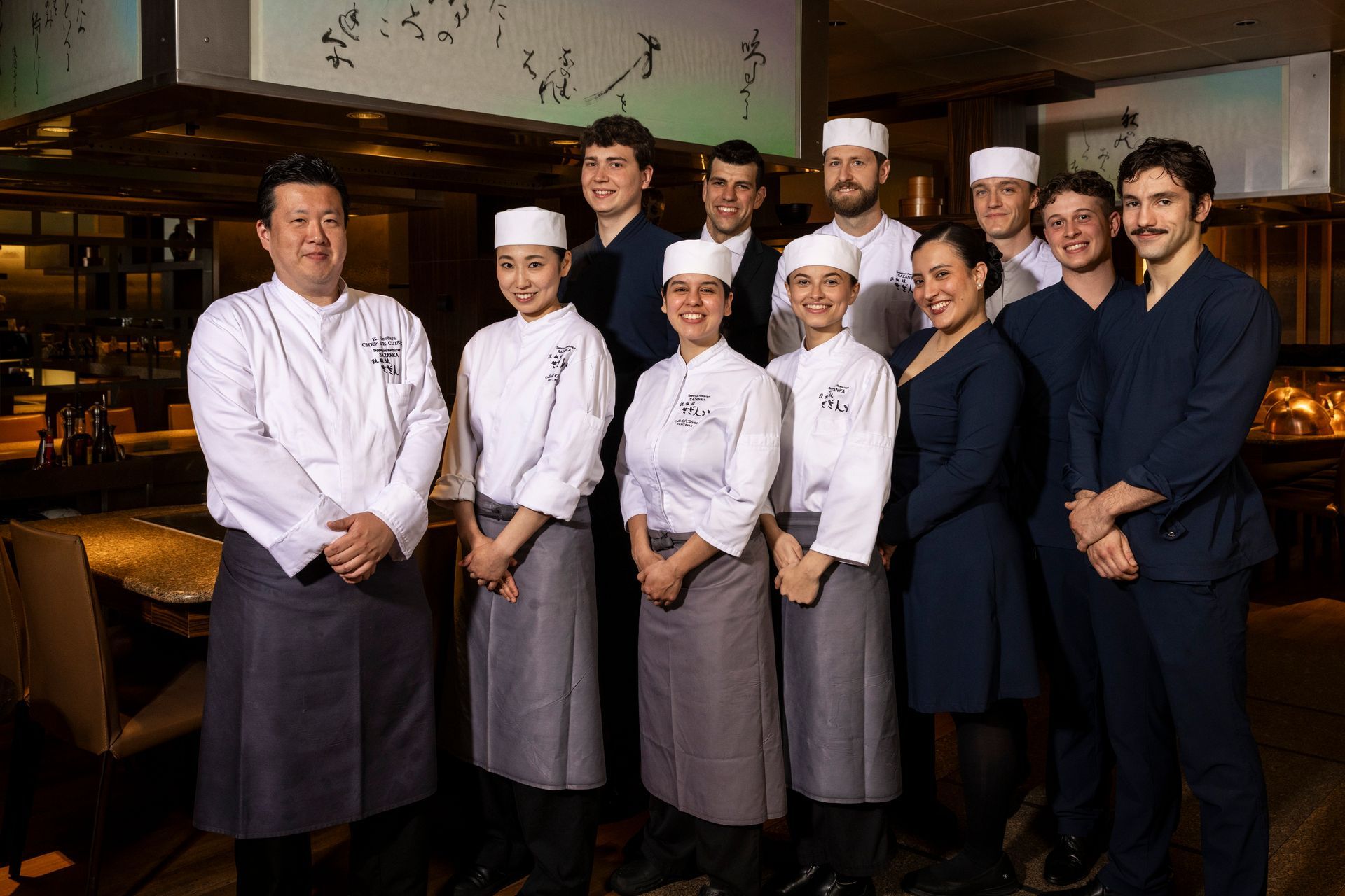 Restaurant staff group photo. Several people in chef whites and formal attire stand together indoors.