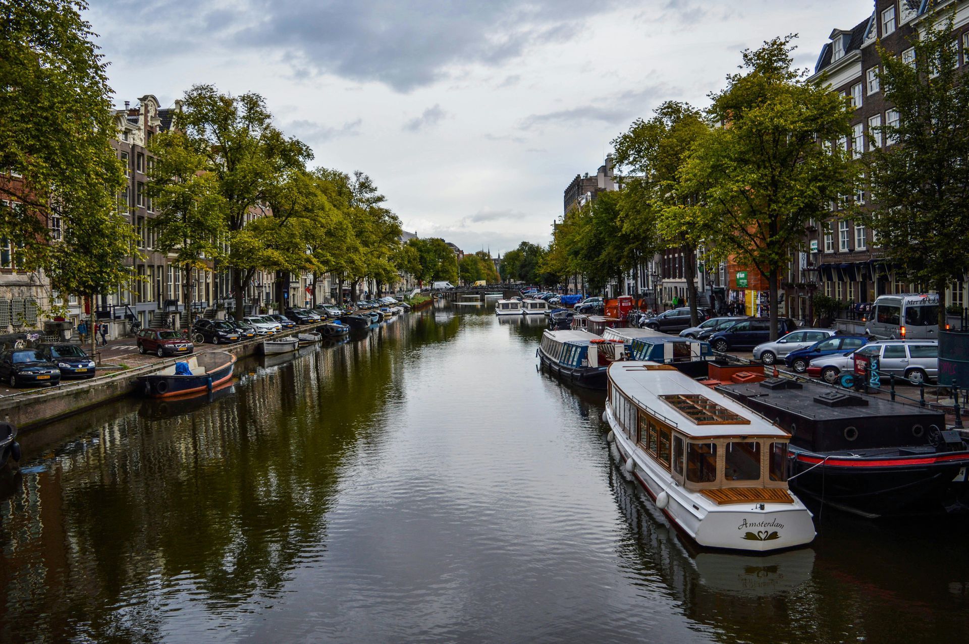 Canal in Amsterdam lined with boats and buildings, under a cloudy sky.