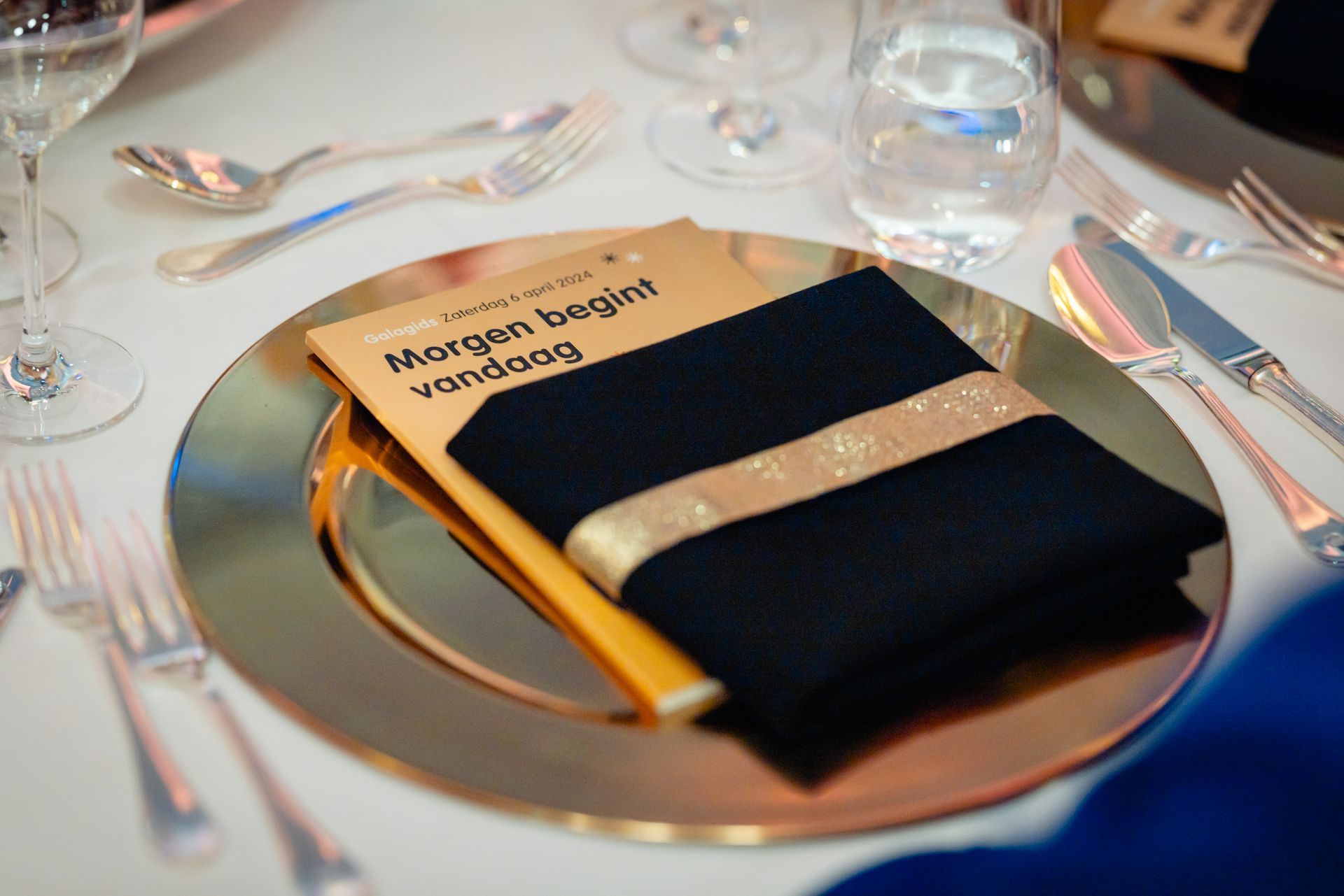 Table setting with gold charger, black napkin with gold stripe, and book.