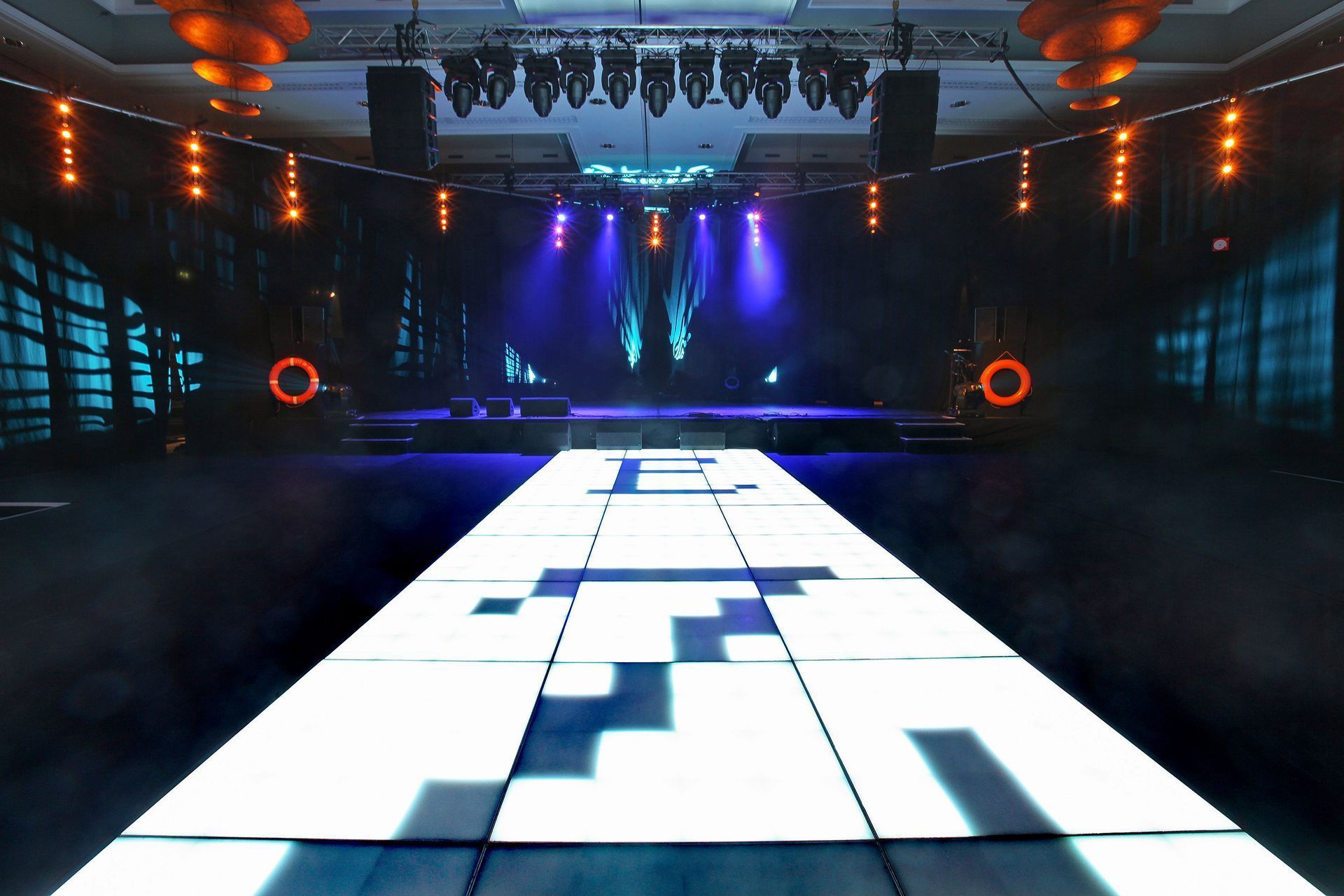 Brightly lit stage with a pixelated runway, dark background, and stage lights.