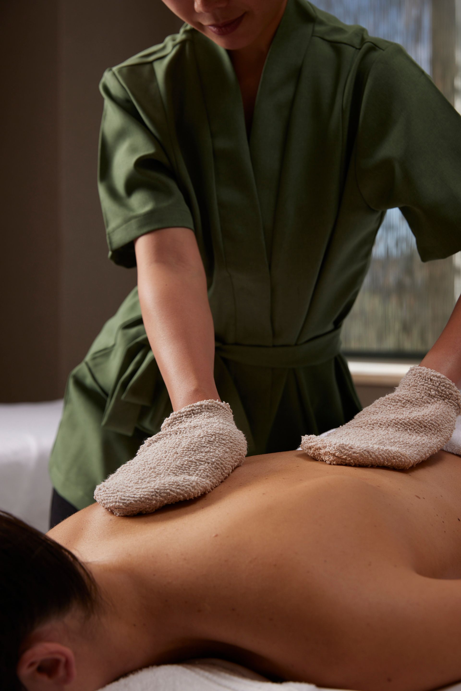 Massage therapist using textured mitts on a person's back in a spa setting.
