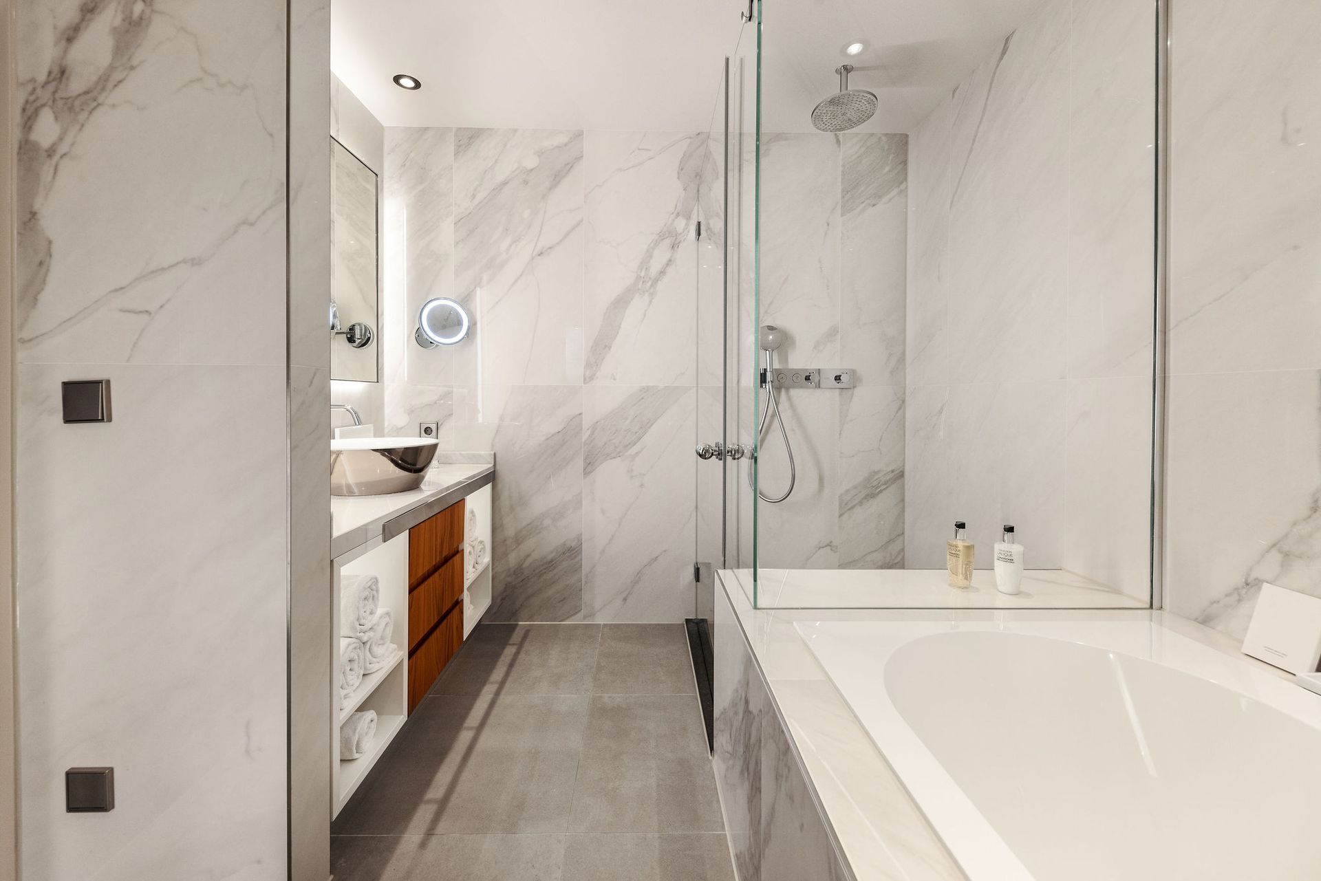 Modern bathroom with marble walls, shower, bathtub, and vanity.