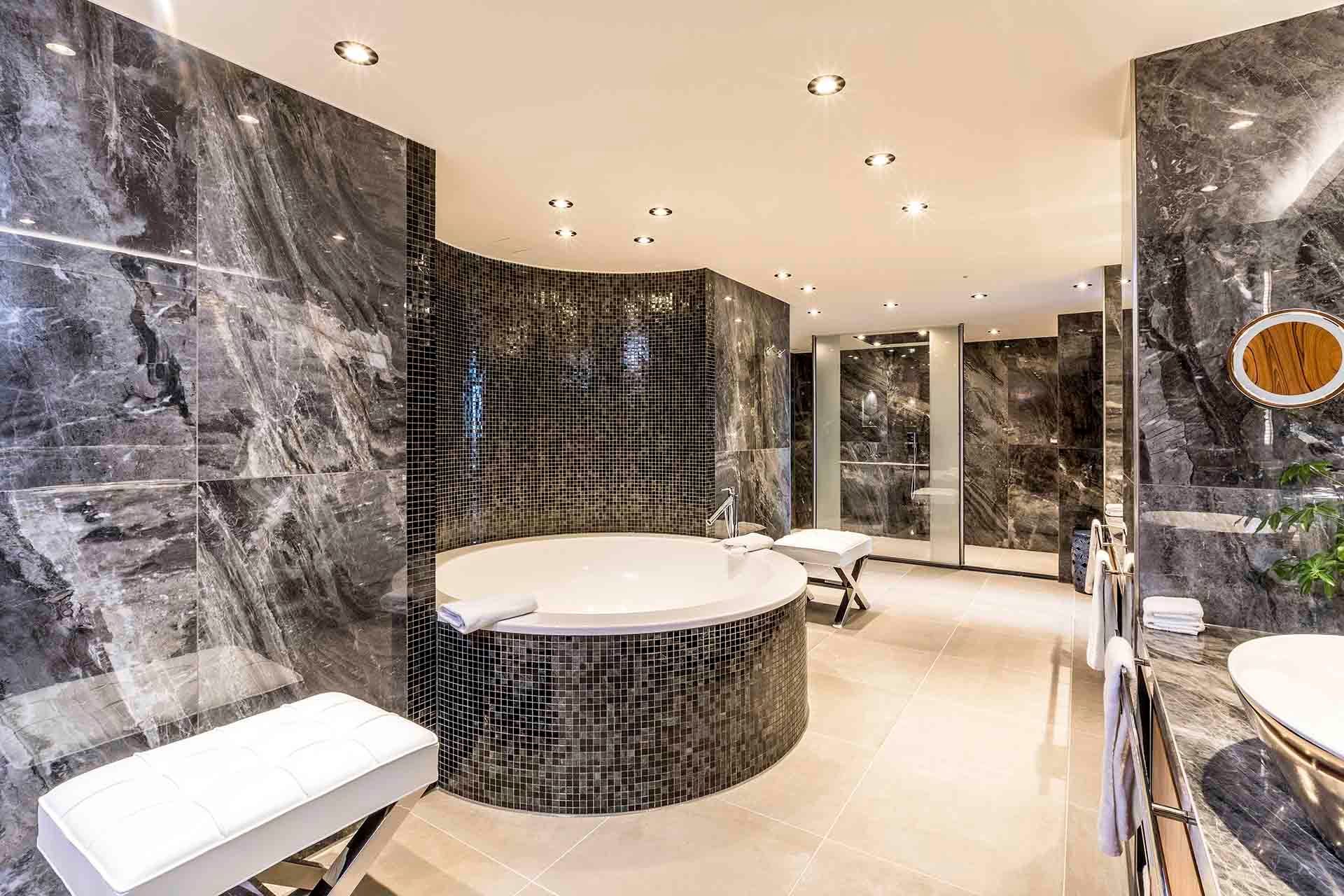 Luxurious bathroom with marble walls, a round tub, and multiple shower stalls.