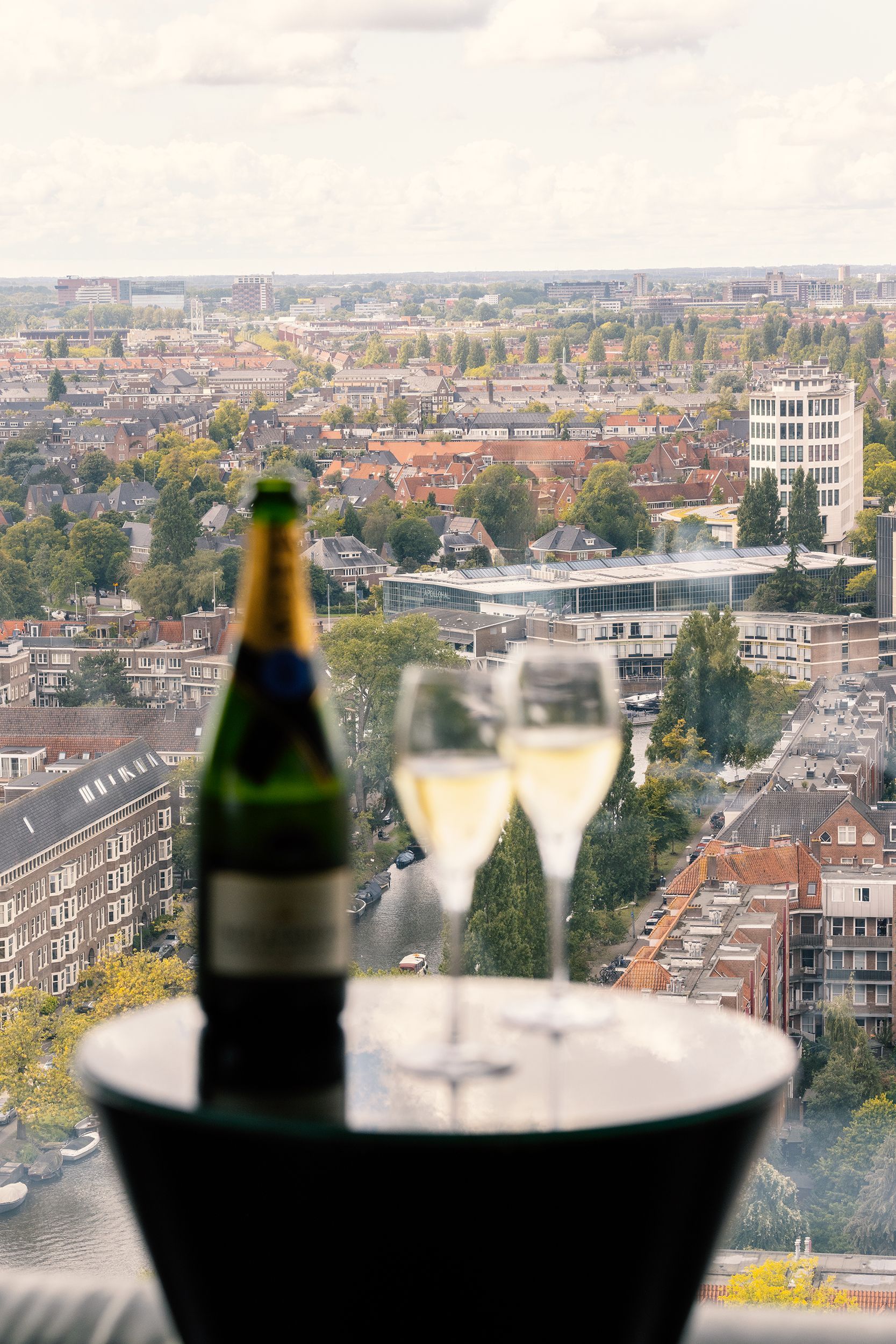 Bottle and two glasses of champagne on a table with a city view in the background.