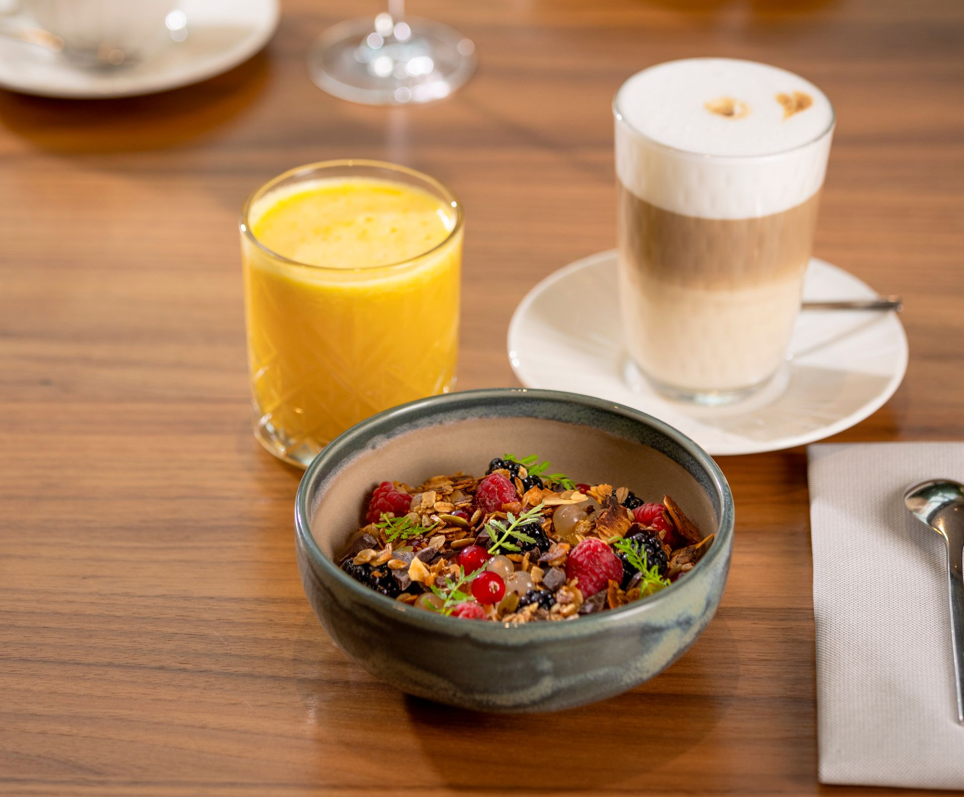 Breakfast table with granola bowl, juice, and latte.