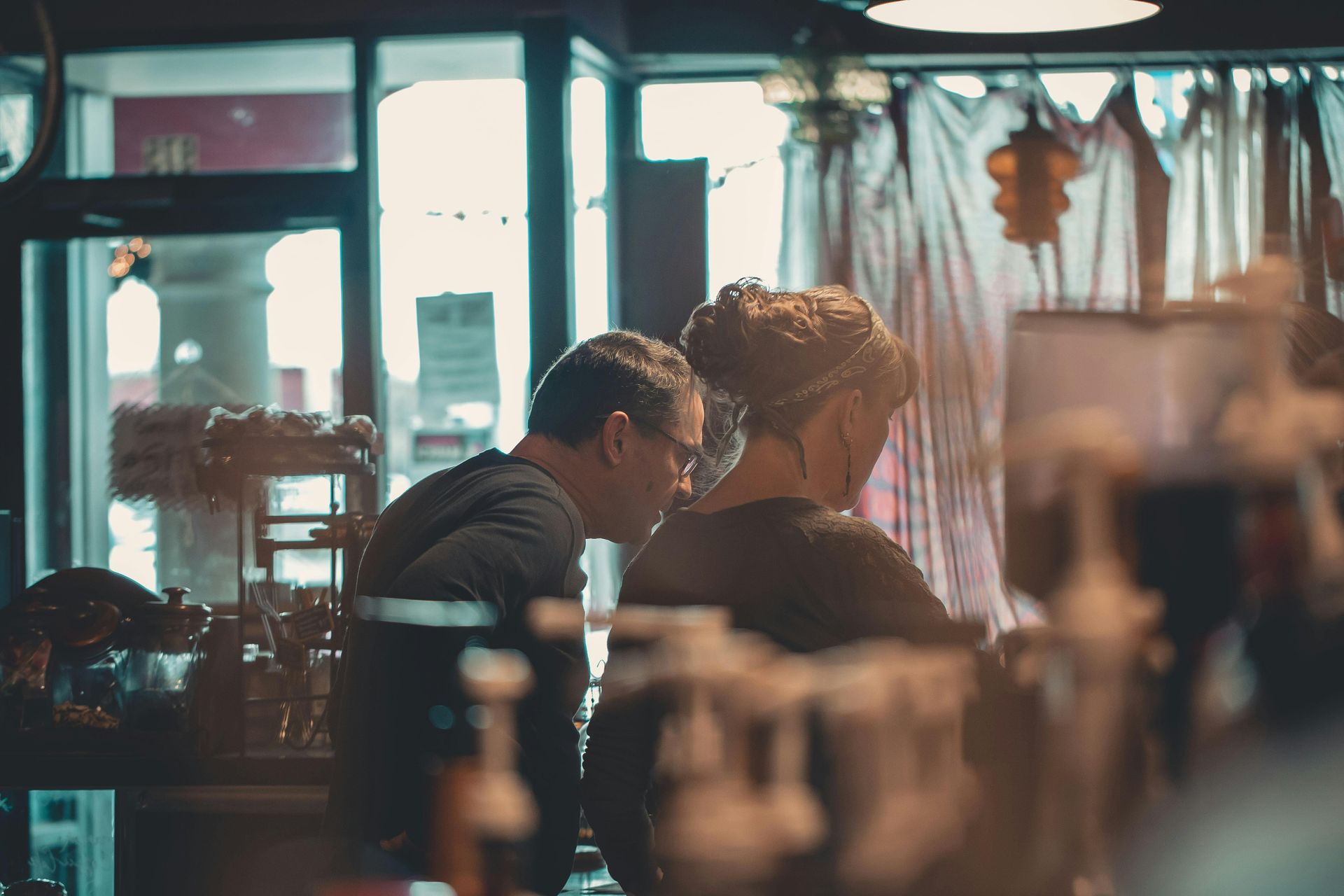 Two people in a shop, looking at items. One is wearing glasses. Soft lighting.