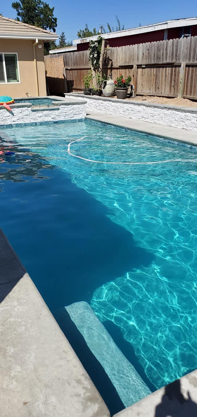 A backyard features a blue swimming pool with a partially covered top, a stone deck, lounge chairs, and a gazebo. A backyard features a blue swimming pool with a partially covered top, a stone deck, lounge chairs, and a gazebo.