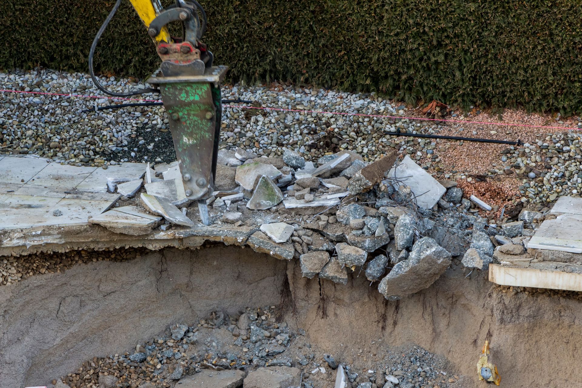 Excavator breaking apart a collapsed concrete slab and rubble at a construction site