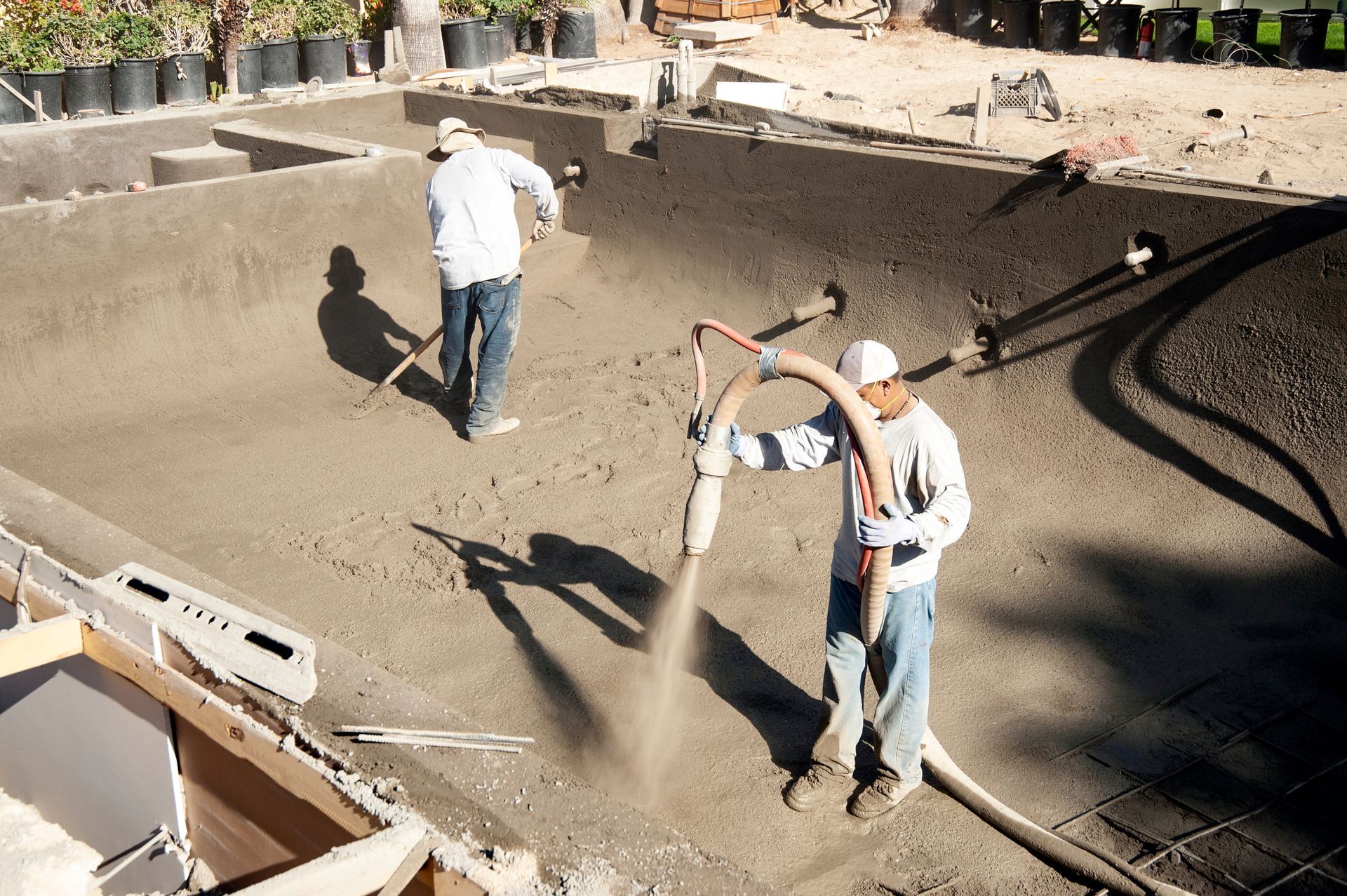 Workers spraying concrete into a large excavation site with hoses and tools