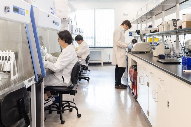 Lab scientists in white coats working in a modern, well-lit laboratory setting.