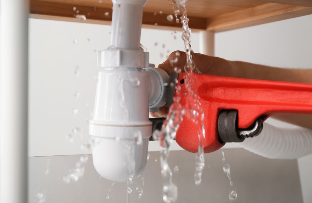 A person is fixing a leaking sink pipe with a wrench.