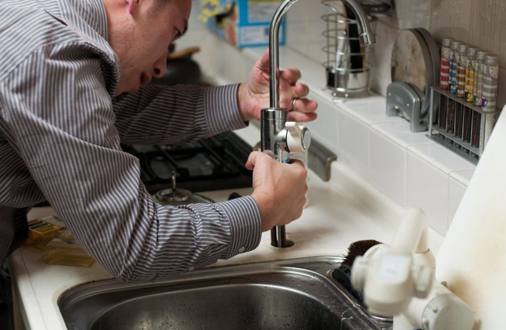 A man is fixing a faucet in a kitchen sink.