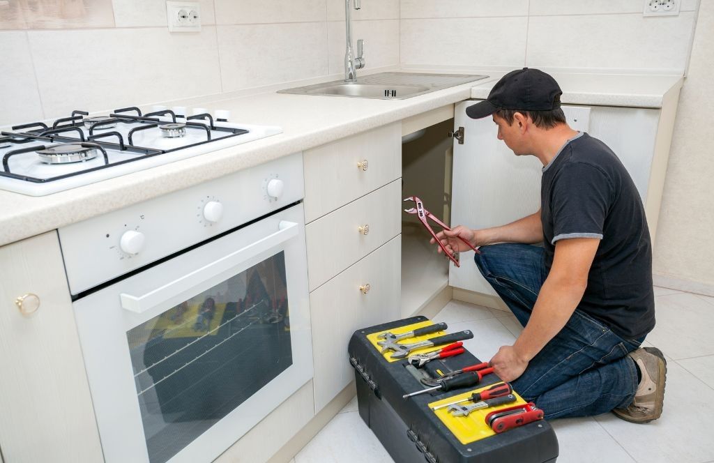 A man is kneeling down in a kitchen with a toolbox.