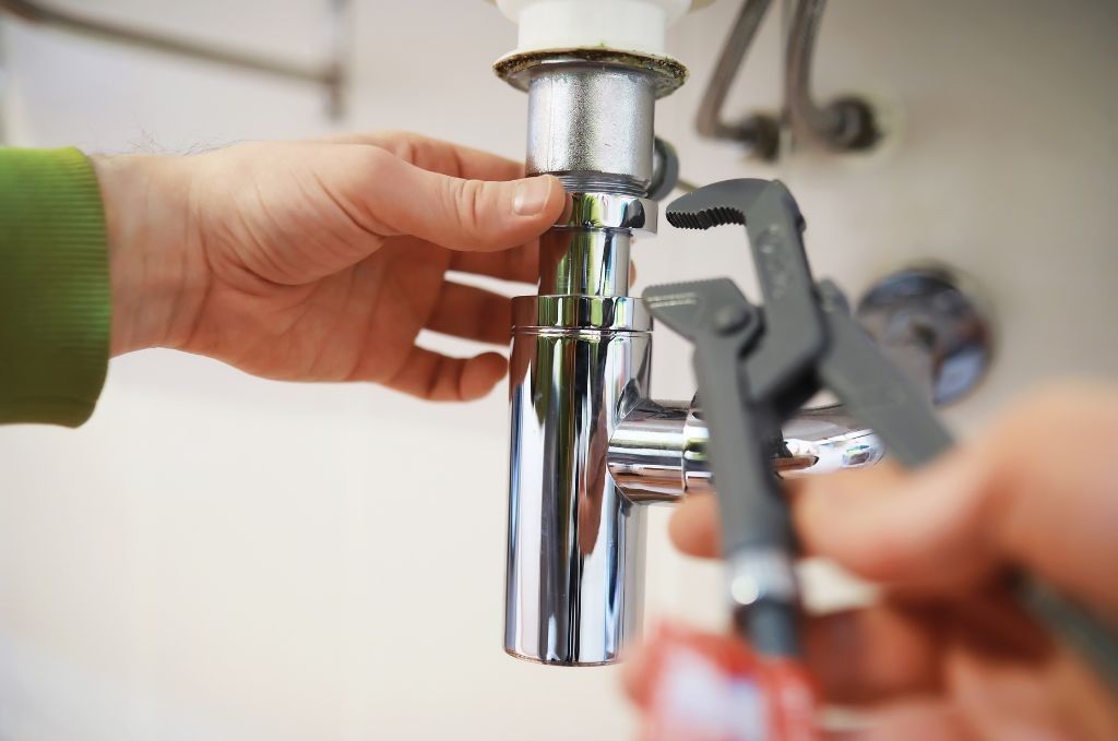 A person is fixing a sink pipe with a wrench.