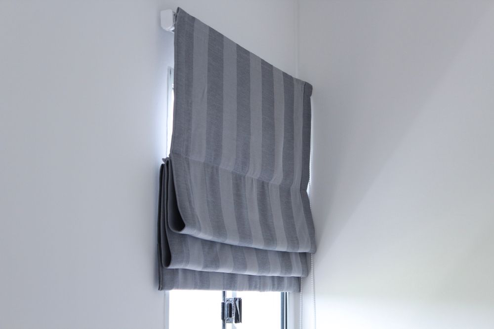 A Grey Striped Roman Shade Is Hanging On A Window — Ulladulla Blinds & Home Improvements In Ulladulla, NSW