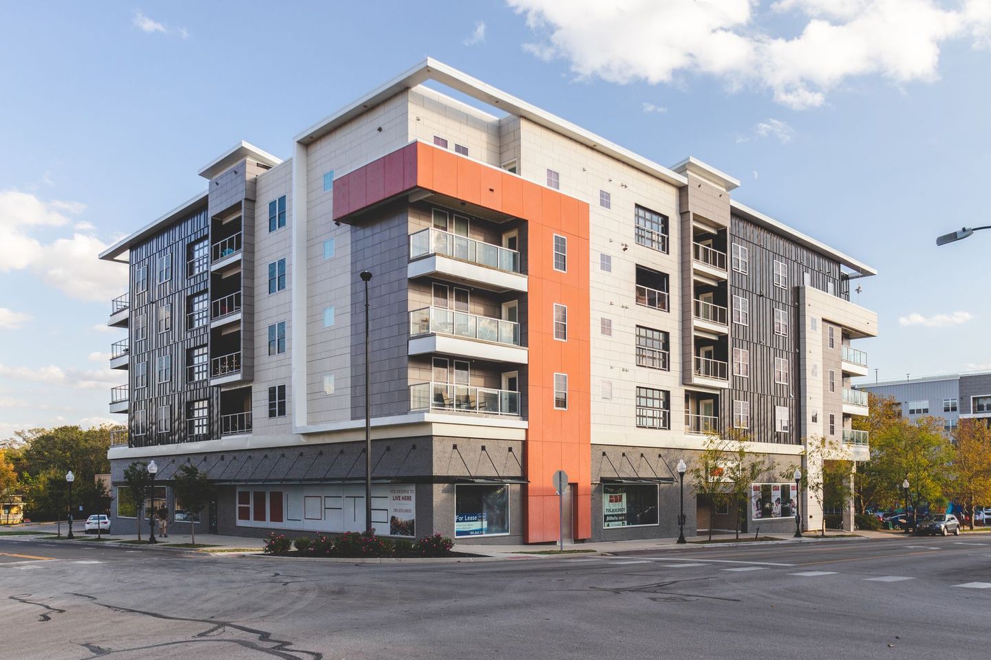 Modern apartment building with balconies and an orange accent wall on a sunny street corner