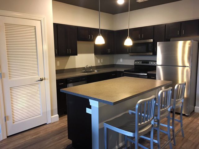 Modern kitchen with dark cabinets, stainless fridge, island, and two metal bar stools