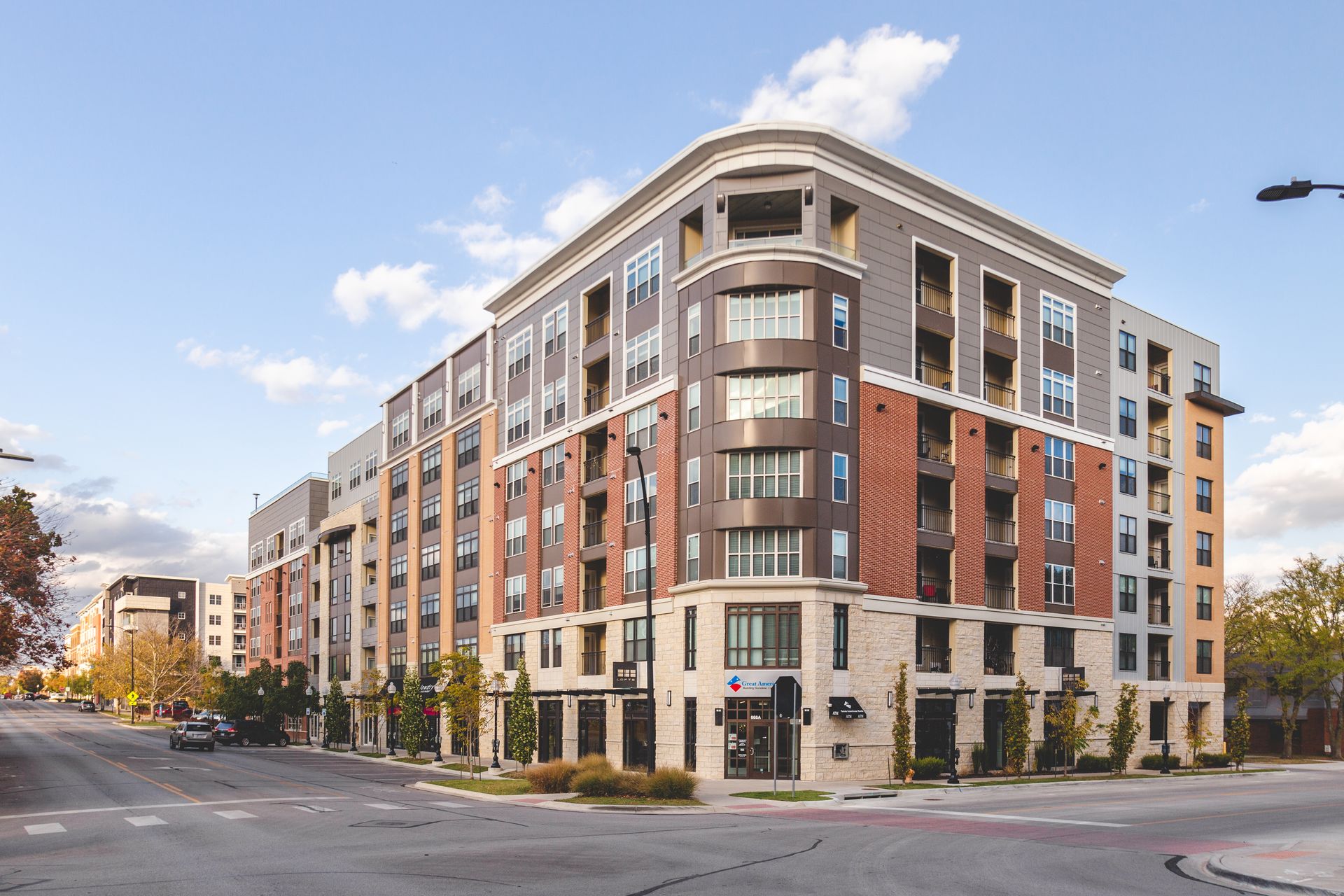 Modern brick-and-stone apartment building on a city street corner under a blue sky
