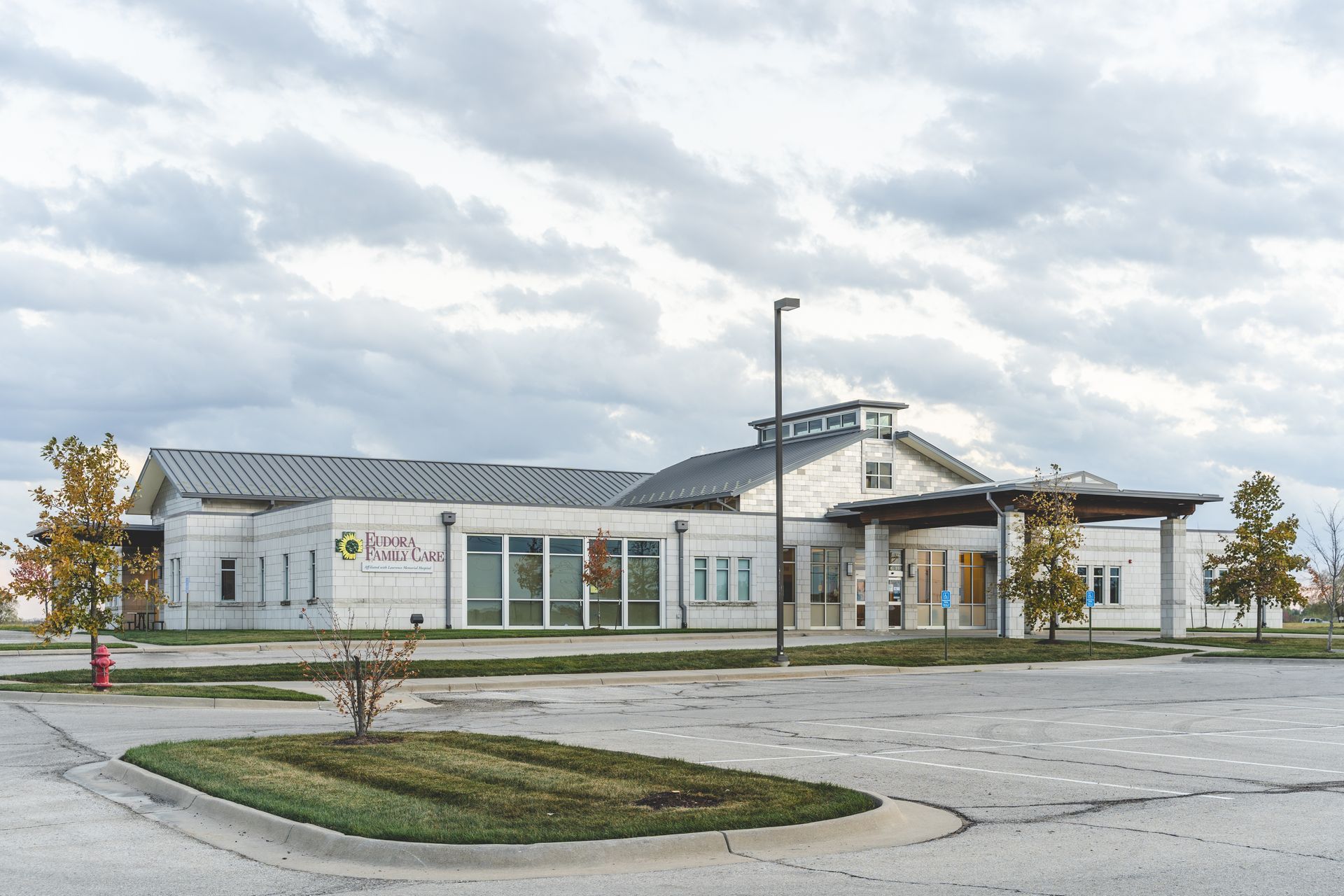 Modern low-rise building with glass entrance, white siding, and empty parking lot on an overcast day