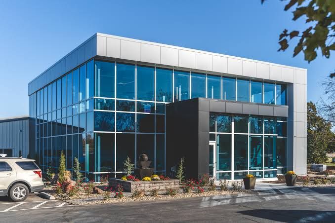 Modern glass office building with blue windows and a parking lot in front