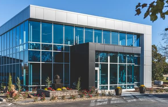 Modern glass office building with a black facade and landscaped entrance under a clear blue sky