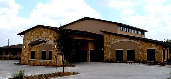 Modern stone-and-wood building exterior with a large covered entrance and parking lot