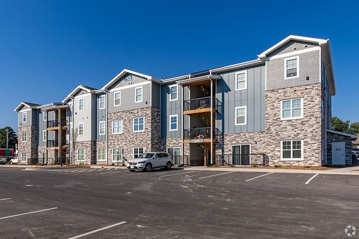 Modern apartment complex with gray siding and stone accents, fronted by a mostly empty parking lot and a parked car
