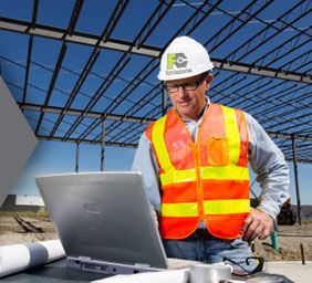 Construction worker in hard hat and safety vest using a laptop at a building site under construction