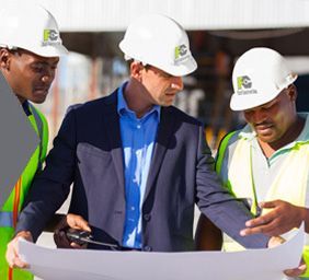 Three construction workers in hard hats reviewing blueprints at a job site