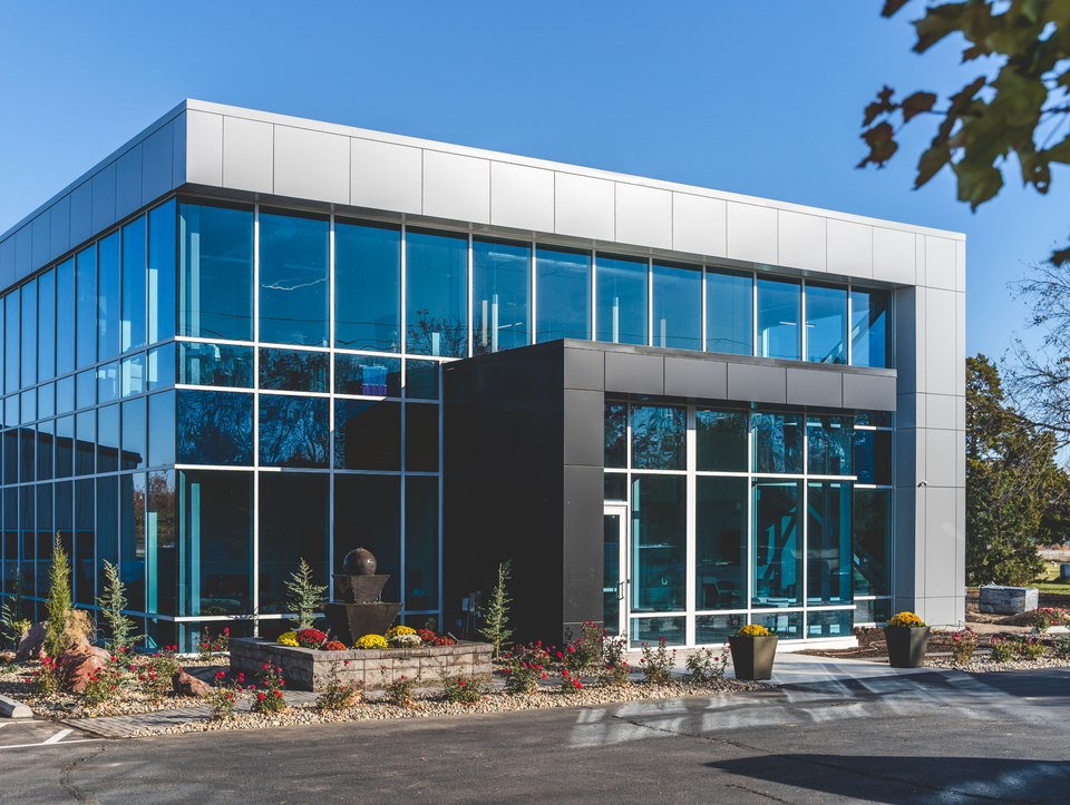 Modern glass-and-steel office building with blue windows and landscaped entrance under a clear sky