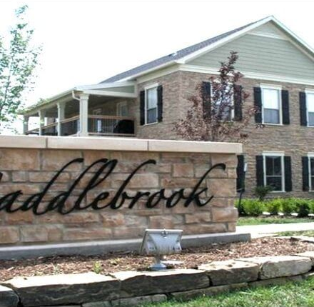 Stone entrance sign reading “Saddlebrook” in front of a brick building with shutters and landscaping