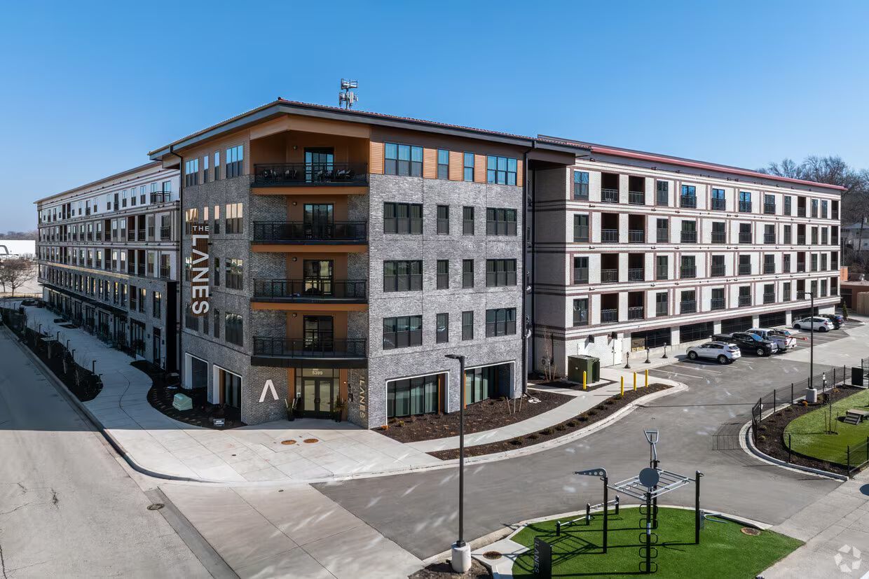 Modern apartment building with stone and wood exterior on a street corner under a clear blue sky