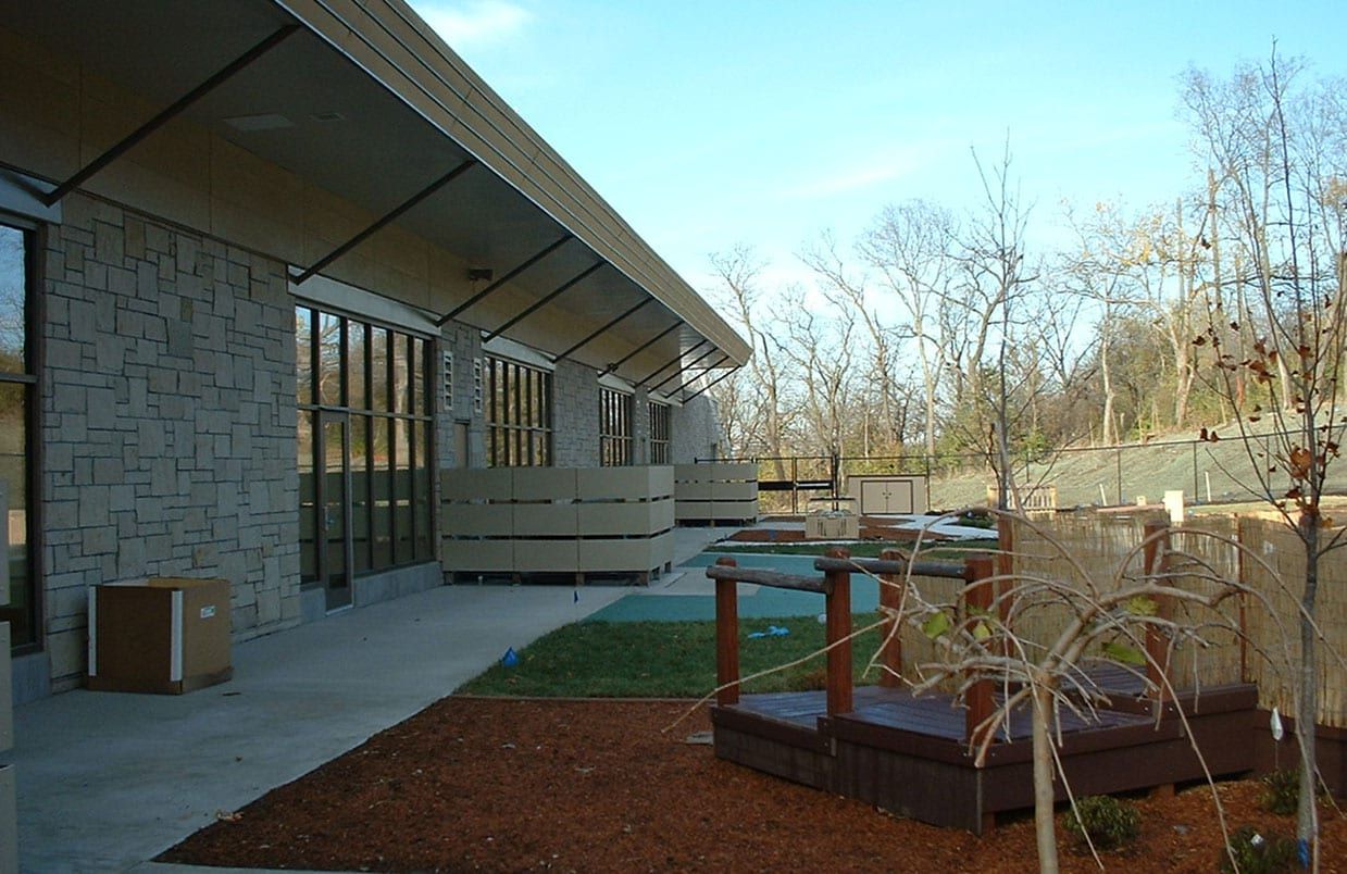 Modern building exterior with a covered walkway, windows, and a landscaped courtyard with raised planters.