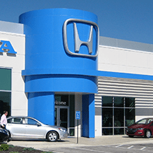 Honda dealership entrance with large blue logo and parked cars outside