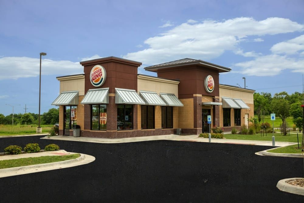 Exterior of a brick fast-food restaurant with striped awnings and a large parking lot under a cloudy sky