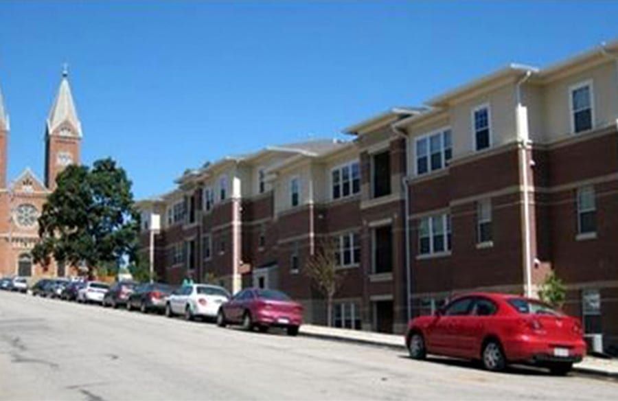 Steep city street lined with brick apartments and parked cars, with a church steeple in the background