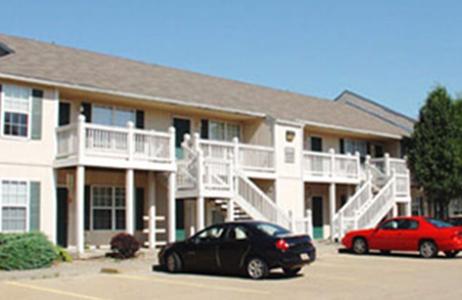 Apartment building with white balconies and two parked cars in front under a blue sky