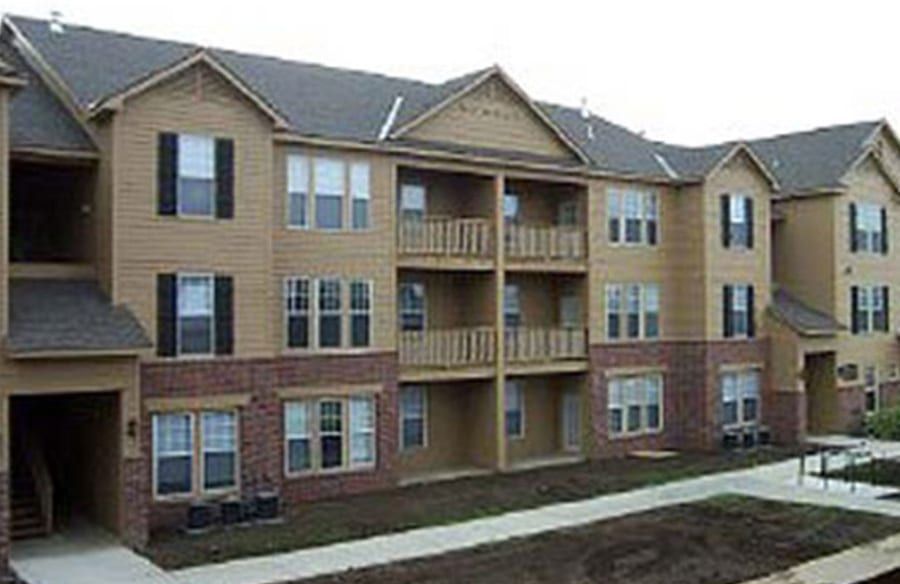 Three-story apartment building with tan and brick siding and balconies along a walkway